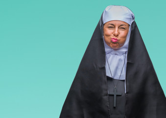 Middle age senior christian catholic nun woman over isolated background puffing cheeks with funny face. Mouth inflated with air, crazy expression.