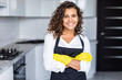 © F8  \ Suport Ukraine - Young american smiling woman wearing apron and rubber gloves, standing in kitchen