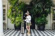 © LUMINA IMAGES - Beautiful Asian woman vacationer standing in front of a hotel with a suitcase and holding her cell phone.