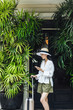 © LUMINA IMAGES - Beautiful Thai woman vacationer standing in front of a hotel with a suitcase and holding her cell phone.