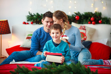 Joyful boy with parents opens New Year's gift box at Christmas home