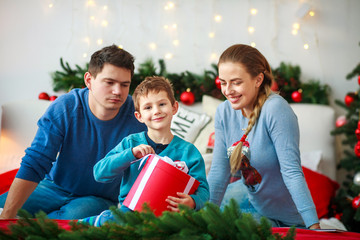 Wall Mural - Joyful boy with parents opens New Year's gift box at Christmas home