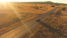 AERIAL: Black SUV Car Driving Along Empty Country Road At Golden Summer Sunset