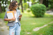 © F8  \ Suport Ukraine - Mixed race Student girl walking while looking her smart phone with the college on park background