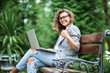 © F8  \ Suport Ukraine - Mixed race woman in eyeglasses sitting on the bench in park with laptop computer and showing thumb up