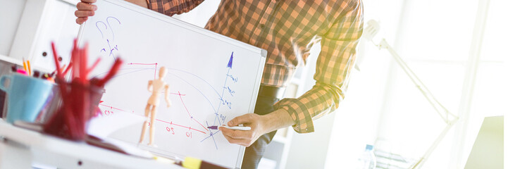 Wall Mural - The man in the office is standing near the table and explains the schedule drawn on the magnetic board.