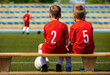 Kids Football Team. Two Young Boys Watching Soccer Match. Football Tournament Competition in the Background. Children Football Team Players in Red Jersey  Uniforms on The Soccer Stadium
