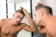 © LIGHTFIELD STUDIOS - adult man adjusting haircut while looking at mirror in bathroom