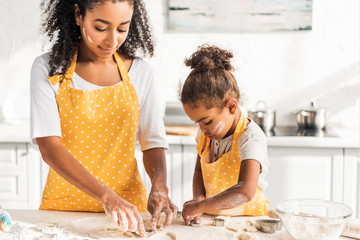 african american mother and adorable daughter preparing cookies with molds in kitchen