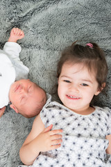 Wall Mural - Little sister hugging her newborn baby brother lying in home bedroom