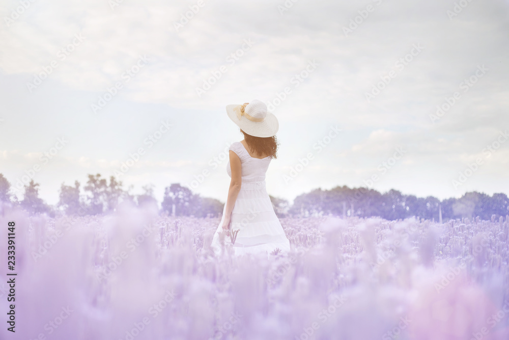 beautiful girl in a white dress and hat in a field of purple flowers ...