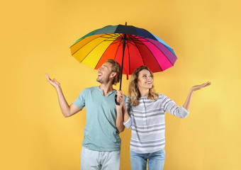 Couple with rainbow umbrella on color background