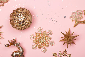 Wall Mural - Golden beautiful sparkling christmas decorative toys on pastel pink background. Flat lay. Festive concept.