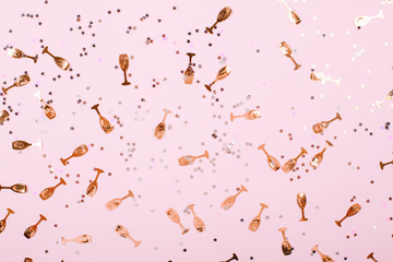 Wall Mural - Party confetti sparkes in gold and white colors. There are small champagne glasses scrattered on the light pink background. Festive concept.