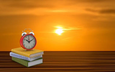 An alarm clock on three books with the sunrise in the background