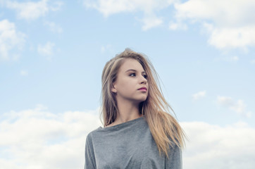 Portrait of a beautiful girl on the background sky. Looks to the right. Youth culture. Fashion for young people. Freedom of choice.