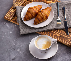 Wall Mural - Croissant, a cup of coffee at wooden tray with napkin on a gray stone concrete table.