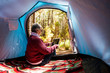 Mature adult retired woman sitting inside a tent in free wild camping alone in the forest using a technology internet connected tablet to organize the travel  for digital nomad work