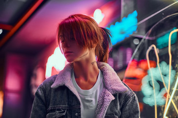 stylish redhead girl standing in the night on the street. illuminated signboards, neon, lights.