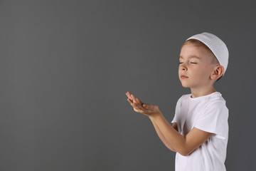 Little Muslim boy praying on gray background. Space for text