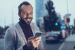 © Yakobchuk Olena - Happy person. Young bearded man in checkered jacket smiling and feeling glad while looking at the screen of his modern smartphone and reading new message
