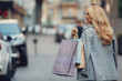 Back view portrait of charming middle-aged lady in stylish jacket carrying shopping bags. She is looking away and smiling