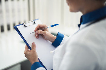 Wall Mural - Concept of professional consultation in healthcare system. Back side close up portrait of female doctor writing on notes holder while standing in cabinet