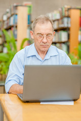 Senior man using laptop in librarySenior man using laptop in library