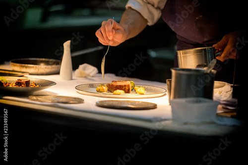 Cuadros en Lienzo Chef preparing a dish with meat on a plate under a light