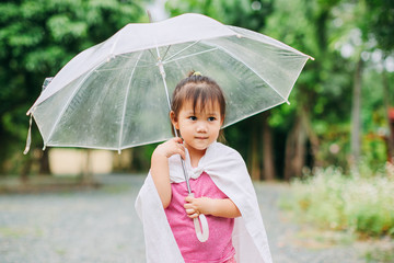 2 years and 9 months kid using umbrella to protect her self from wetting the rain that can cause of sickness from cold or the flu. Concept for rainy season.