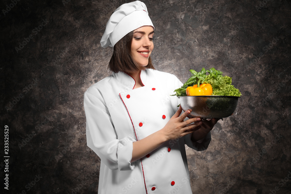 Young female chef with vegetables on dark background