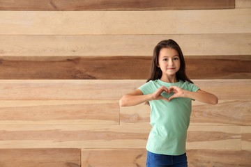 Canvas Print - Cute girl in t-shirt making heart with her hands on wooden background