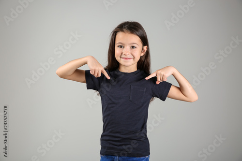 Cuadros en Lienzo Cute girl pointing at her t-shirt on light background