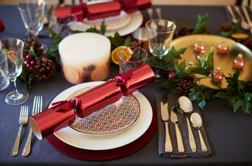 Close up of Christmas table setting with crackers arranged on plates and red and green table decorations, close up