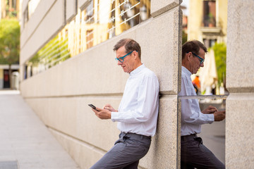 Smiling attractive stylish mature man using smart phone in urban outdoors city
