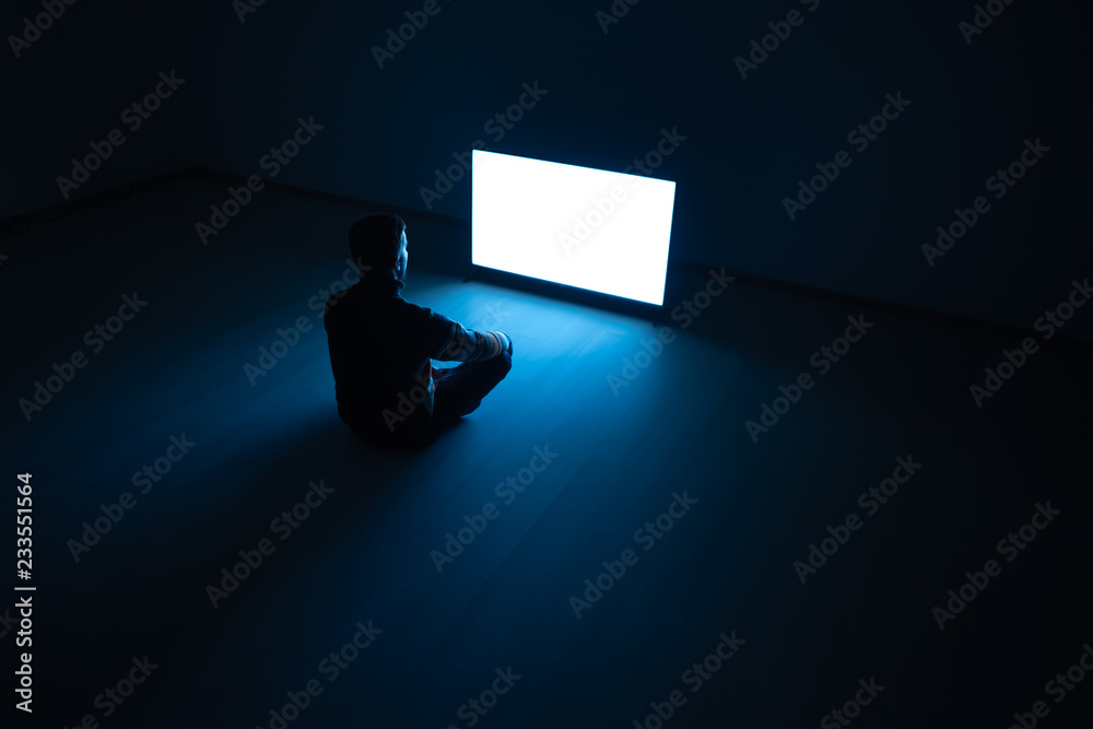 The man sitting in the dark room in front of a white screen
