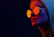 Neon close up portrait of young woman in round sunglasses and hoodie. Studio shot