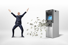 A Happy Businessman Stands On A White Background Near An ATM Machine With Many Dollar Banknotes Flying Around.