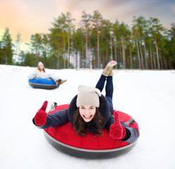 Sticker - winter, leisure and entertainment concept - happy teenage girl sliding down hill on snow tube and showing thumbs up over natural background