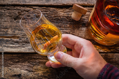 Fotomural hand holds whiskey in a glass for tasting on a wooden background
