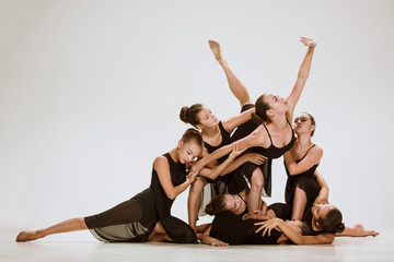 The group of modern ballet dancers dancing on gray studio background