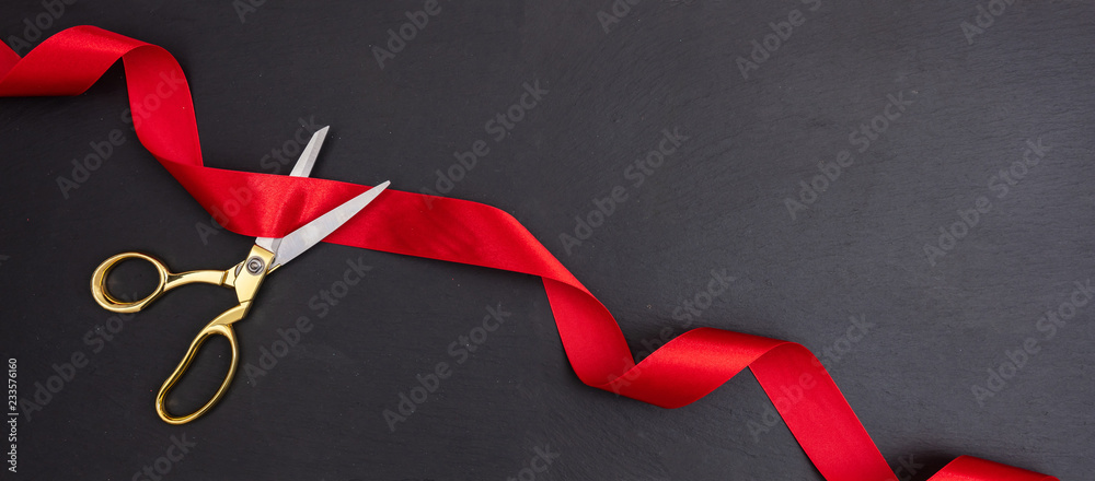 Scissors cutting red silk ribbon against black background, banner. - obrazy, fototapety, plakaty 