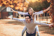 © Mediteraneo - Couple having fun man giving piggyback to woman in autumn park