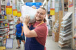 Young bearded salesman carries a pack of plaster on his shoulder in counstruction store