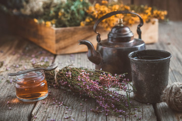 Wall Mural - Vintage teapot, cup of healthy herbal tea, small honey jar,  heather bunch and medicinal herbs on background.
