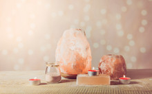 Himalayan Salt Soap Bar, Pink Rock Salt Lamp Turned On And Salt Candle Holder, With Candle Burning Inside, Jar With Salt Grains On Light Bokeh Background, Studio. Calming Zen Moods Concept.