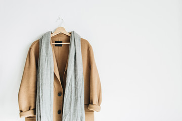 Beige woolen female coat and grey scarf on hanger at white wall. Woman fashion winter cloth concept.