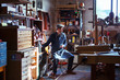 © Cavan for Adobe - Carpenter holding drink looking away while sitting on stool in workshop