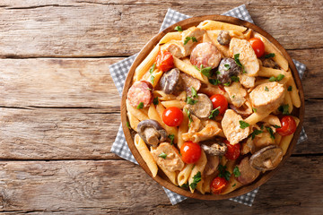 Italian penne pasta with chicken fillet, mushrooms, smoked sausage, cayenne pepper covered with cream cheese sauce close-up. horizontal top view