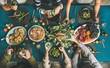 © sonyakamoz - Company of friends of different ages gathering for Christmas or New Year party dinner at festive table. Flat-lay of human hands holding glasses with drinks, feasting and celebrating holiday, top view